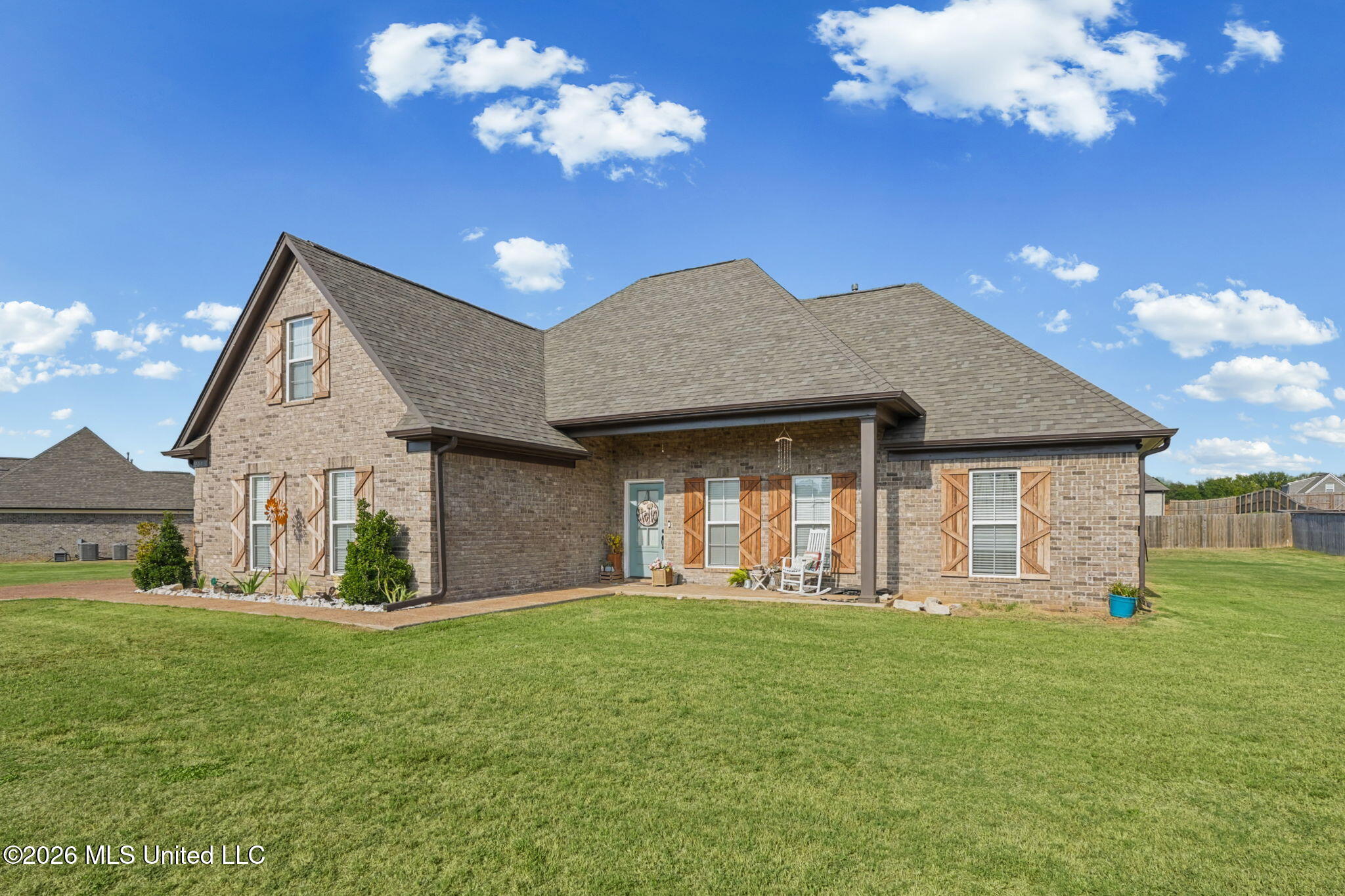 Brick house with wood shutters, covered porch, and broad green lawn.