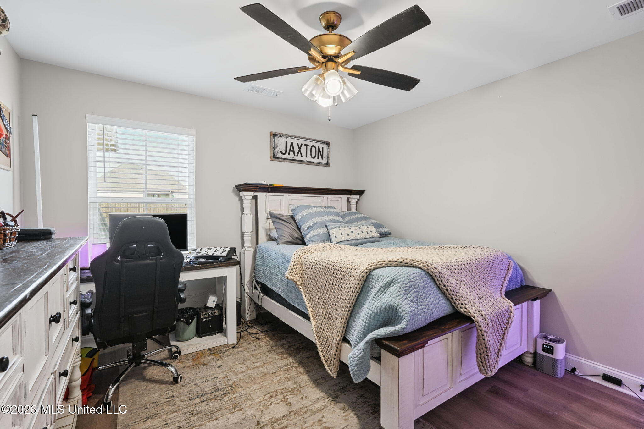 Furnished bedroom with blue bedding, a knitted throw, and a desk beside the window.