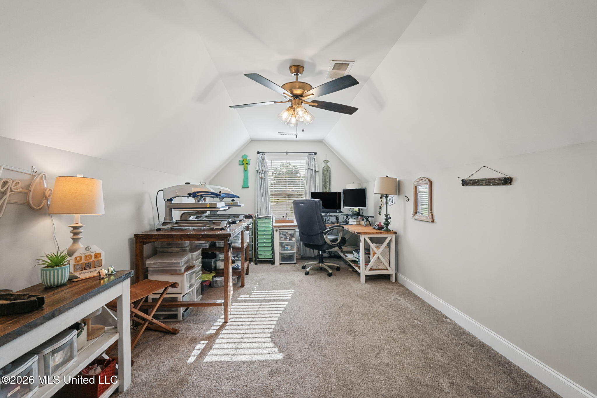 Home office with vaulted ceiling, two desks, computer monitors, and craft equipment.