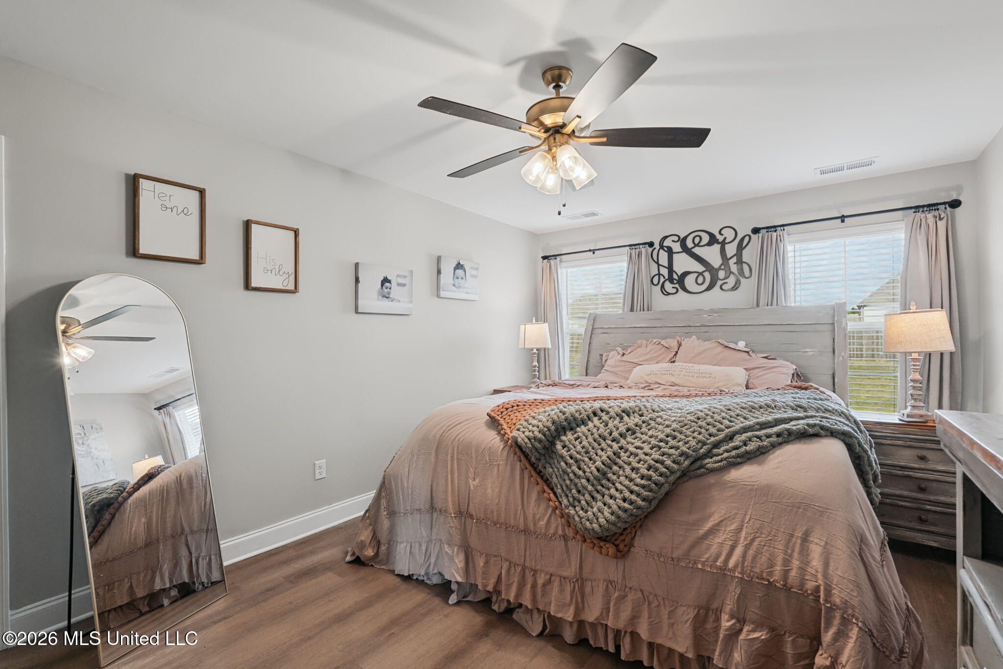Bedroom with blush bedding, a chunky gray throw, a gray headboard, and a ceiling fan.