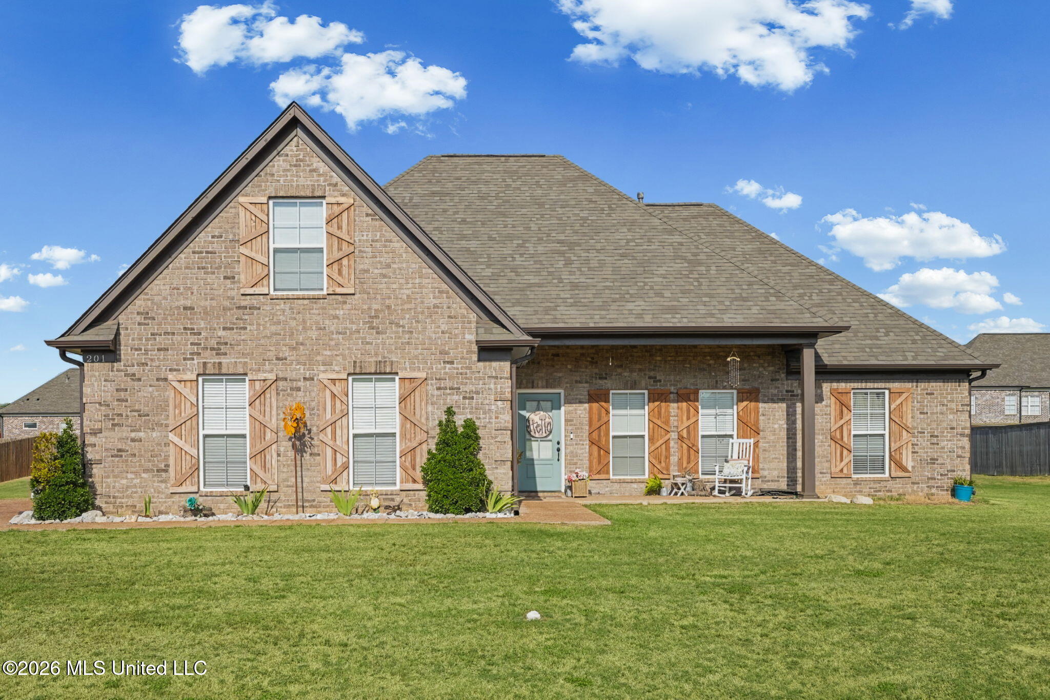 Brick house with wood shutters, a covered porch, and a broad green lawn.