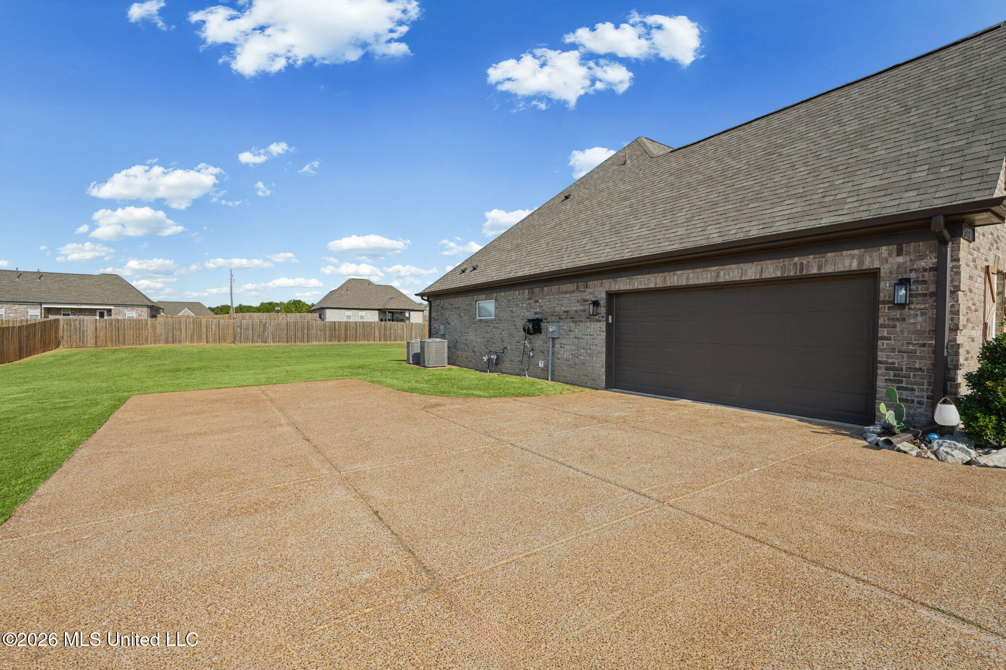 Brick home with a large double garage, wide concrete patio, and fenced lawn.