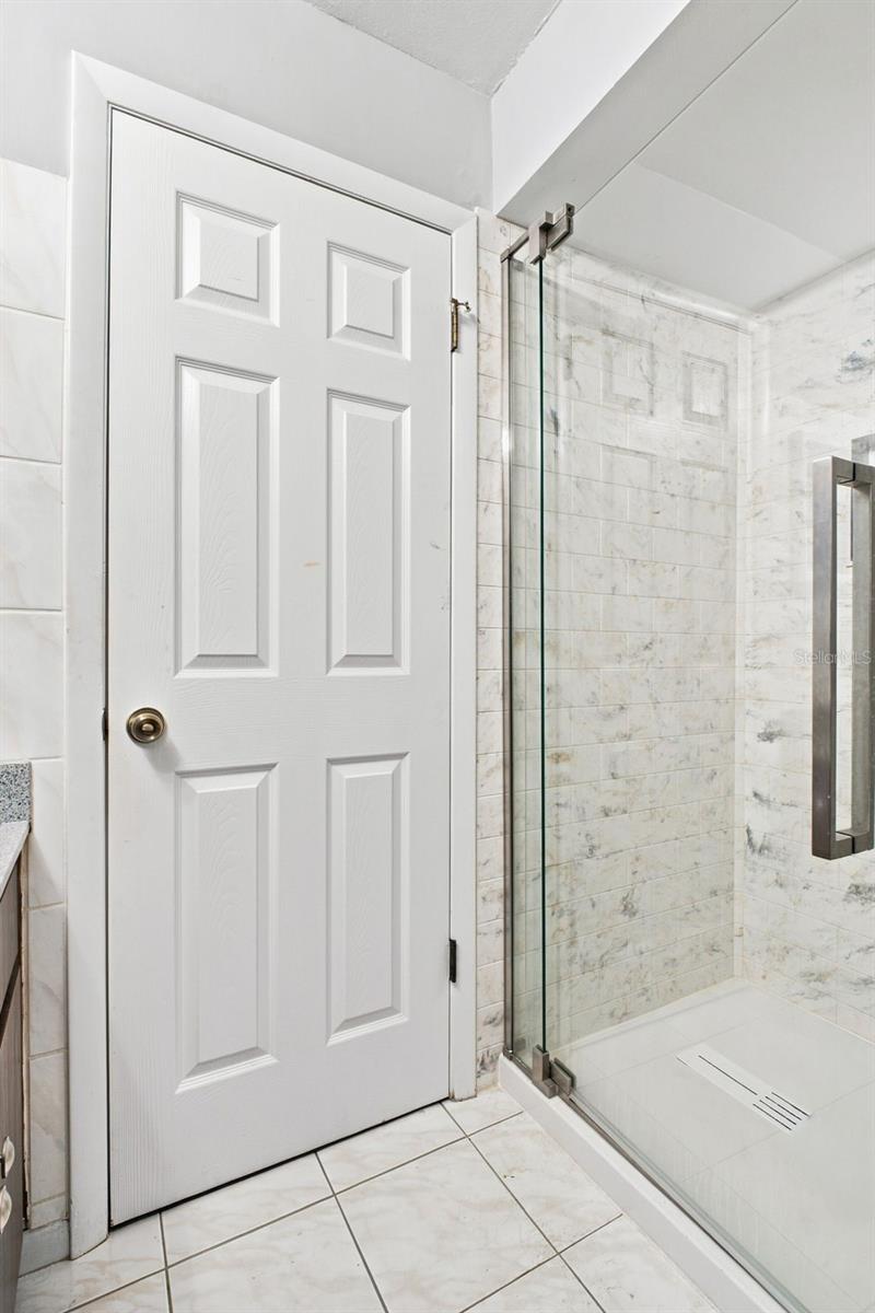 Bathroom with a marble-look tiled walk-in shower and glass enclosure beside a white paneled door.