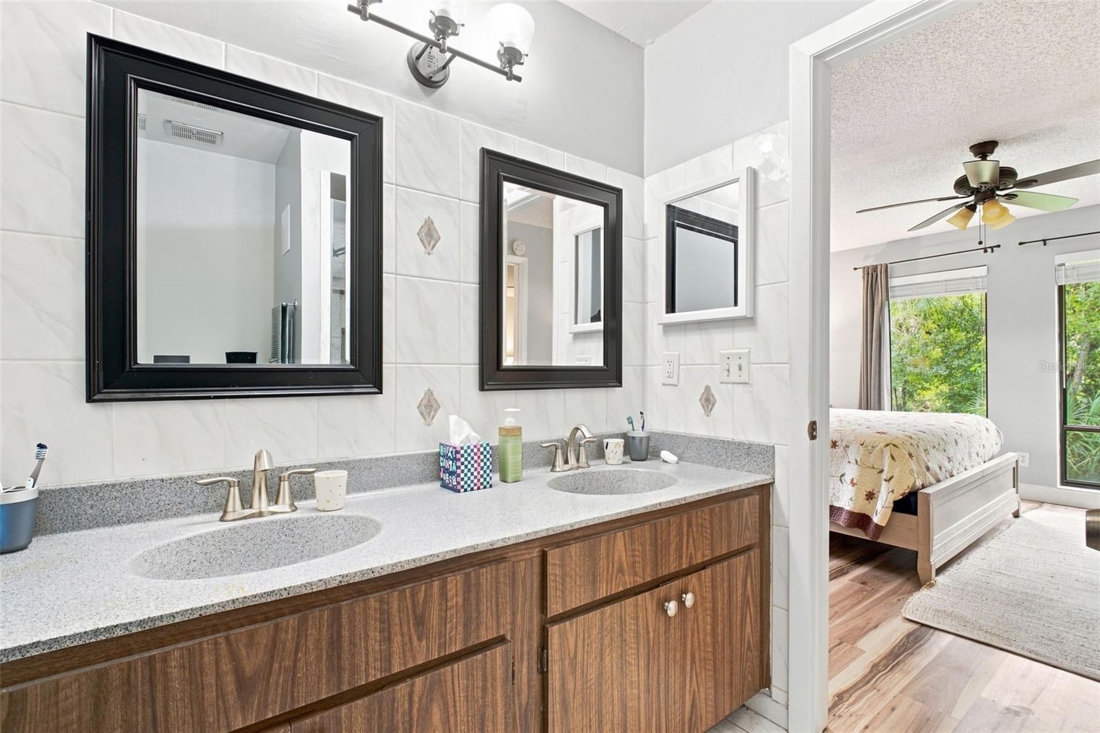 Bathroom vanity with two sinks and black-framed mirrors, opening to a bright bedroom.