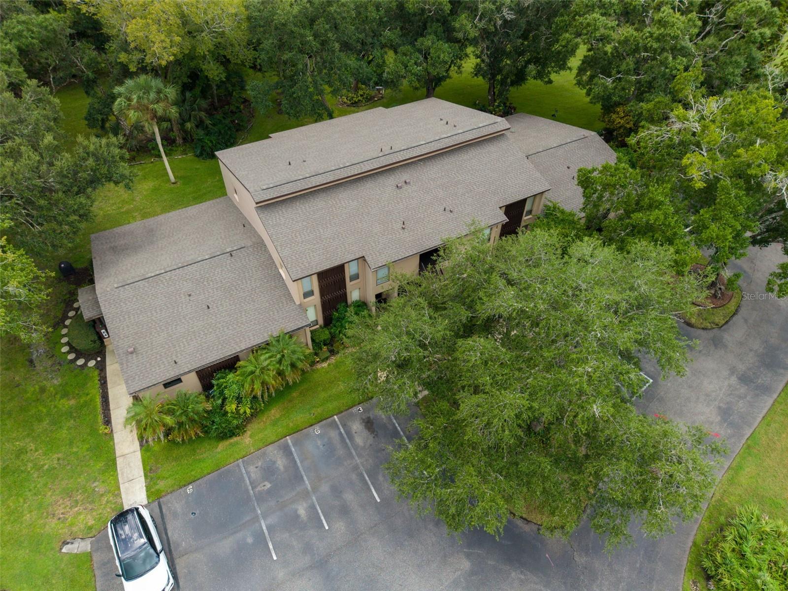 Aerial view of a residential building surrounded by trees, lawns, and a parking lot.