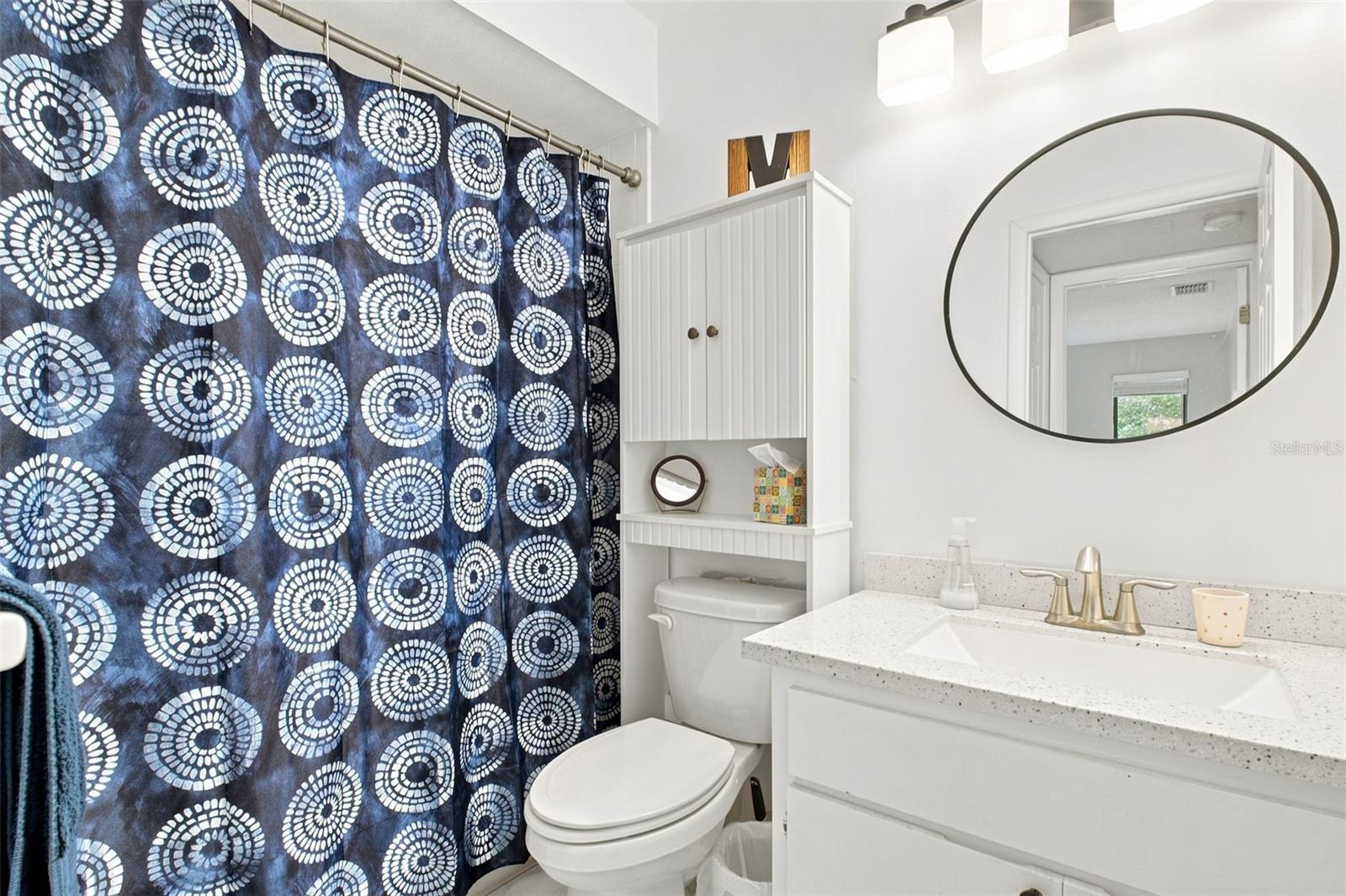 Bathroom with a speckled white vanity, oval mirror, and navy patterned shower curtain.