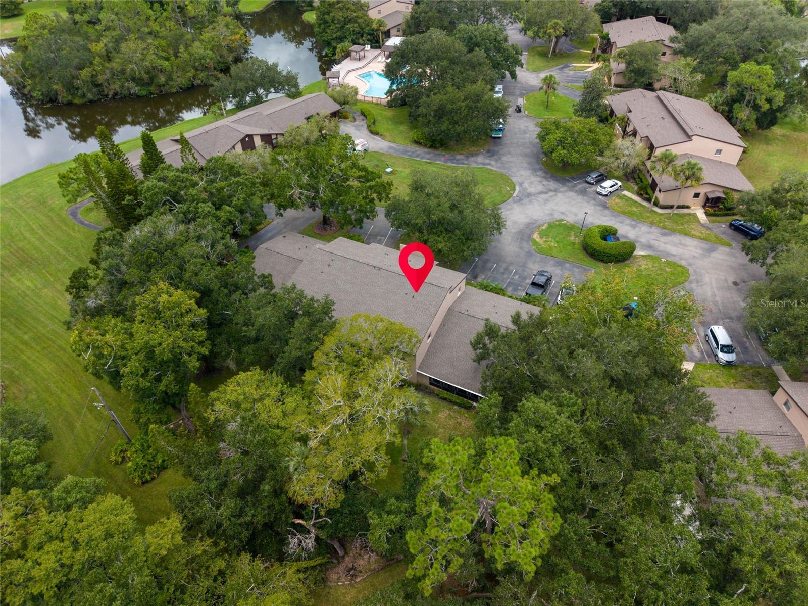 Aerial view of a tree-lined condominium community, with a red marker identifying one building near a pond and pool.