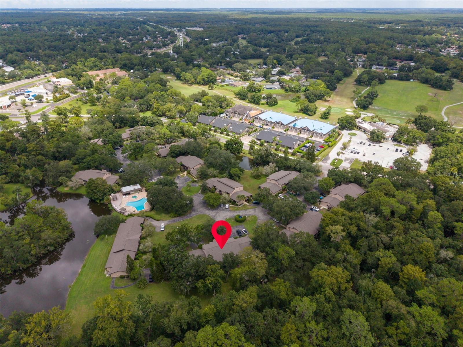 Aerial view of a wooded community, with a red pin marking a home near ponds, a pool, and golf fairways.
