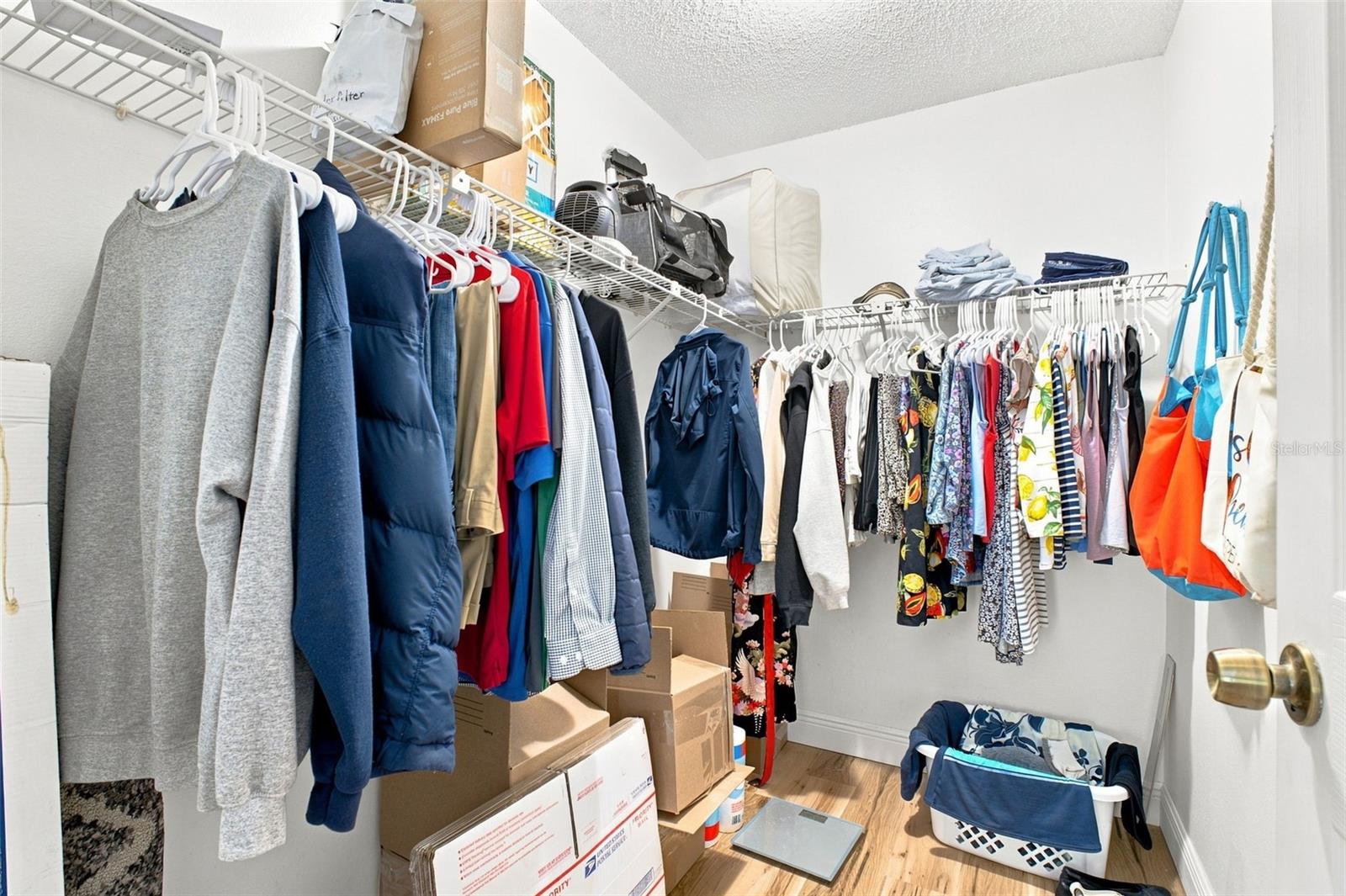 Crowded walk-in closet with clothes on wire shelving and boxes stacked below.
