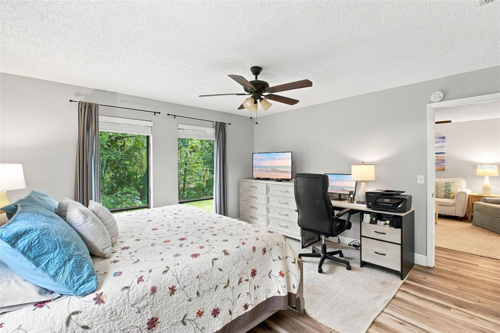 Bedroom with a floral quilted bed, leafy window views, and a desk workspace.