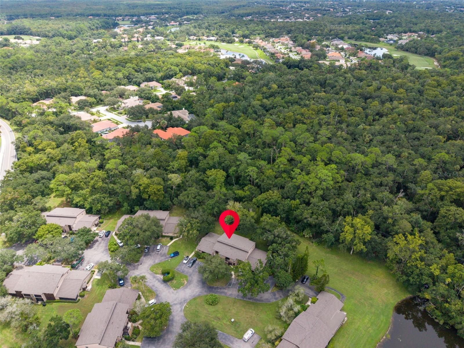 Aerial view of a marked residential building amid dense trees, with a golf course in the distance.