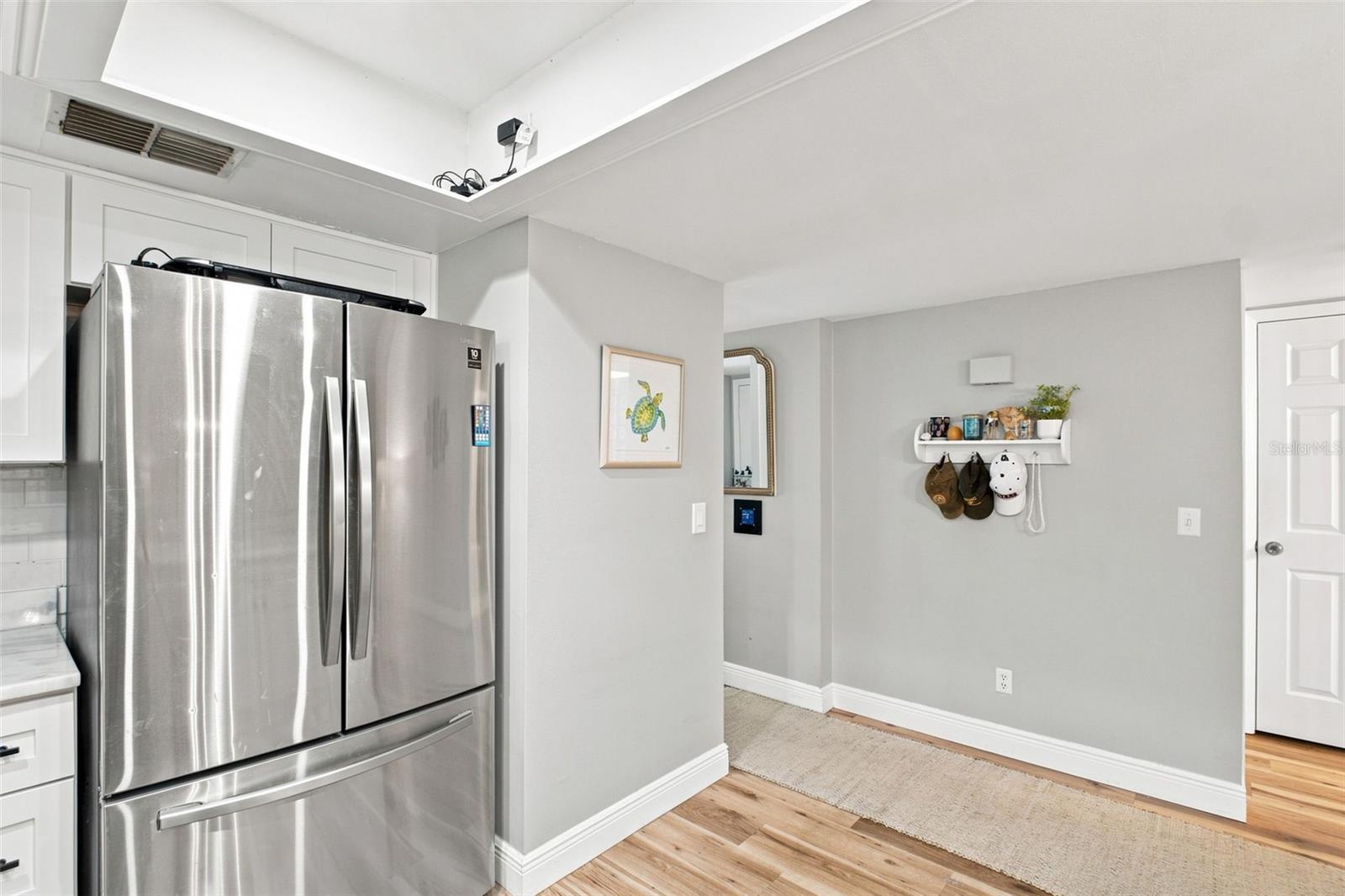Kitchen with a stainless steel refrigerator, white cabinets, and wood flooring.