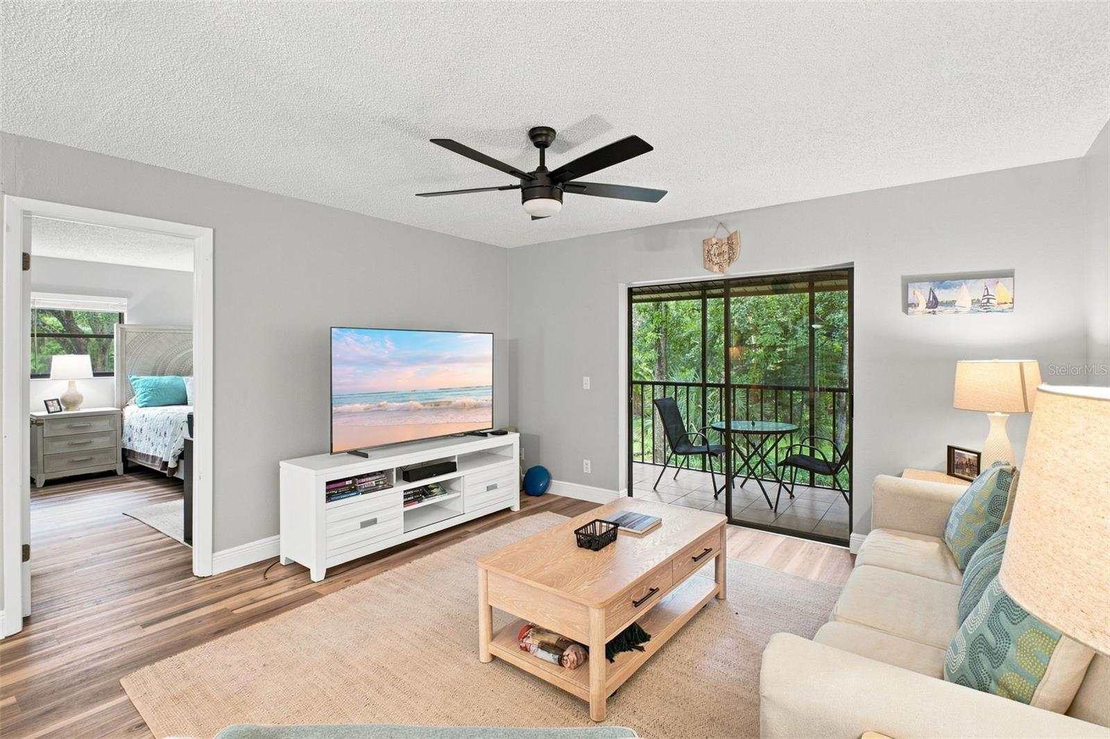 Living room with a cream sofa and sliding glass doors overlooking greenery from a screened balcony.