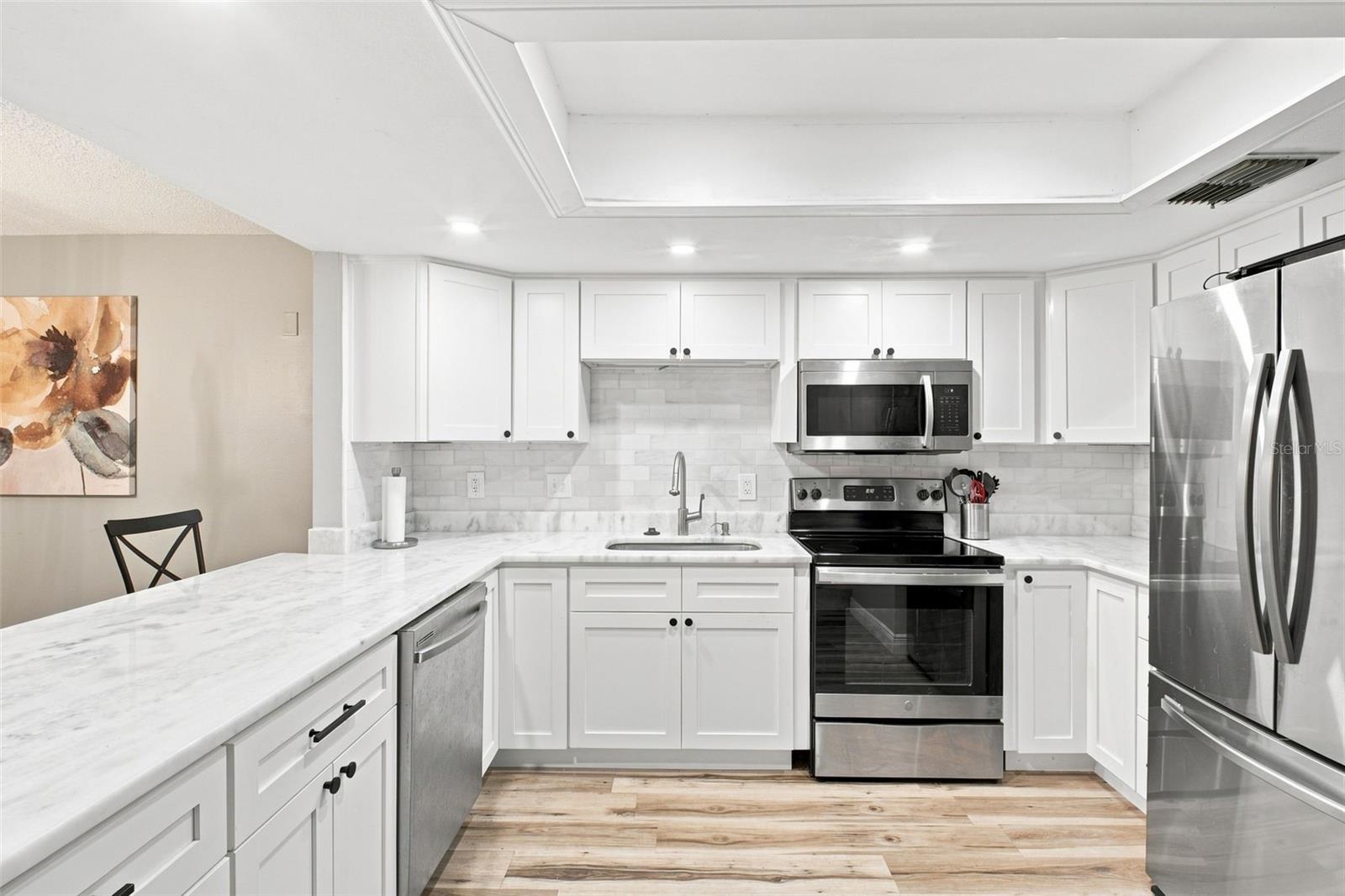 Renovated kitchen with white cabinets, marble-look counters, and stainless steel appliances.