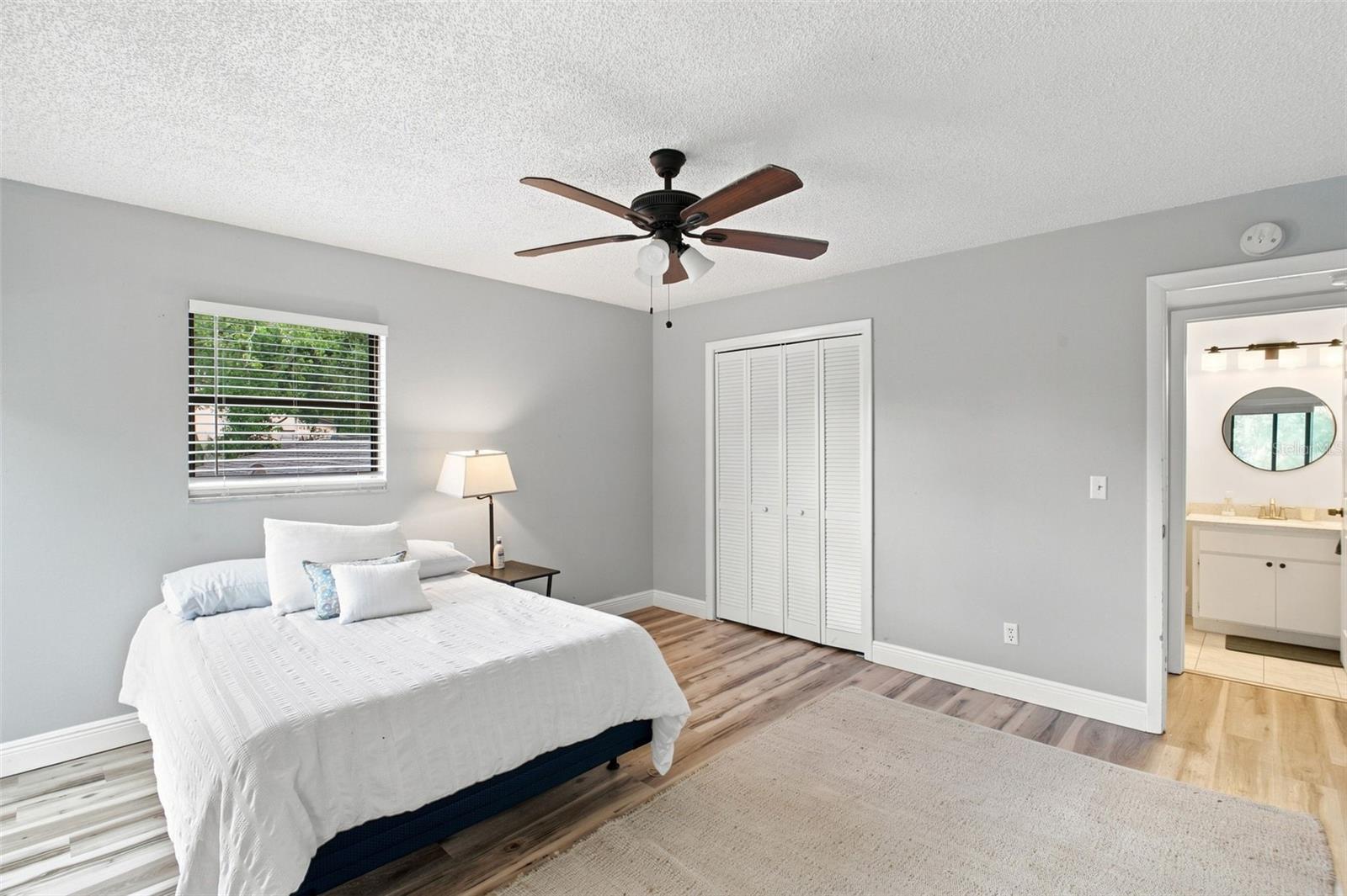 Bedroom with a white bed, ceiling fan, closet, and adjoining bathroom.