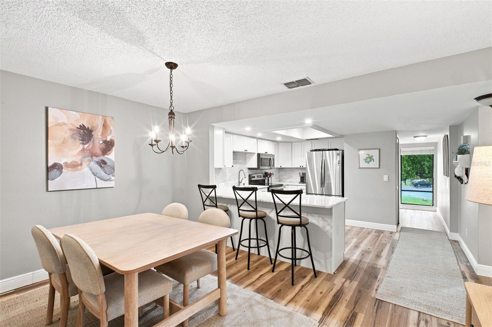 Dining area opens to a white kitchen with a marble island and stainless appliances.