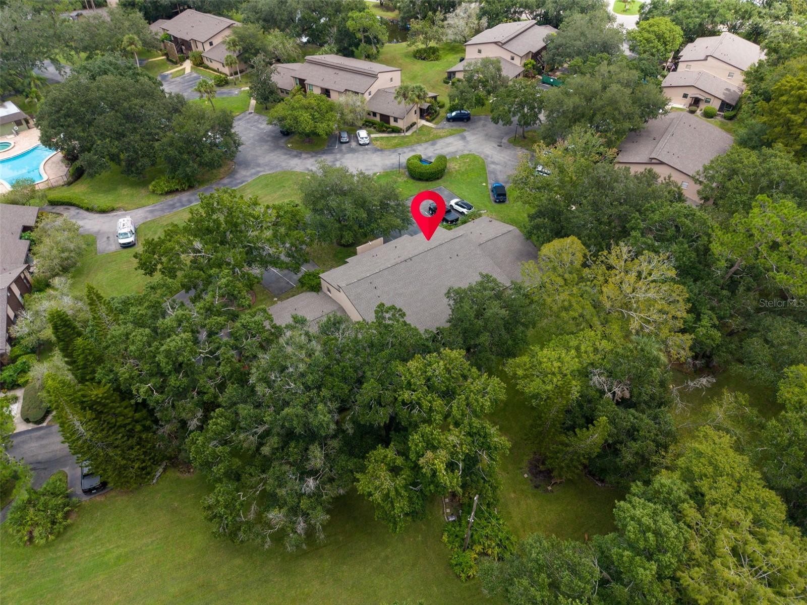 Aerial condos with a red pin marking one building among trees and a swimming pool.