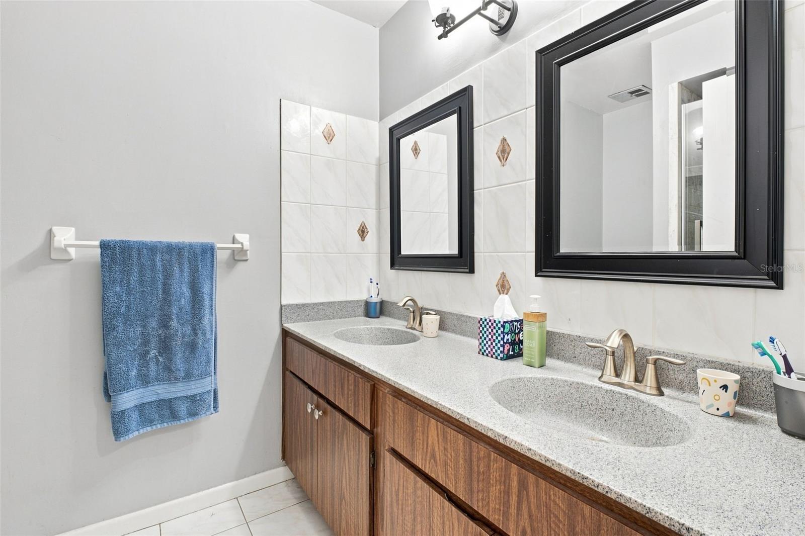 Bathroom with a double-sink wood vanity, speckled countertop, and black-framed mirrors.