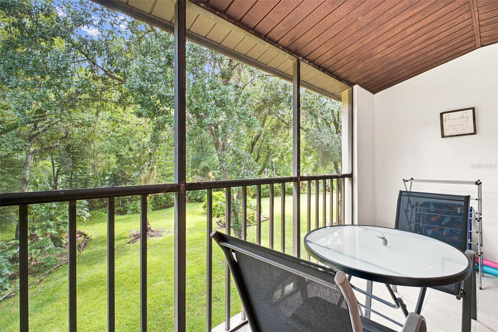 Screened patio with a glass-top dining table overlooking a lawn and mature trees.