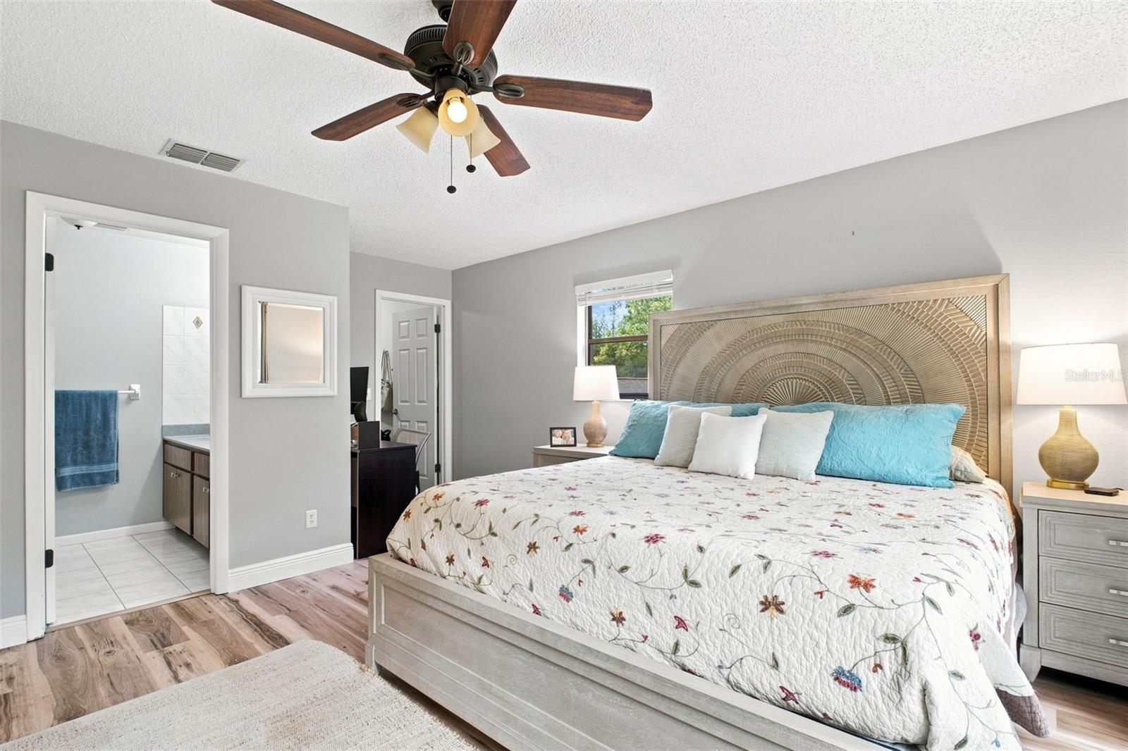 Furnished bedroom with a floral quilt, turquoise pillows, ornate headboard, and attached bathroom.