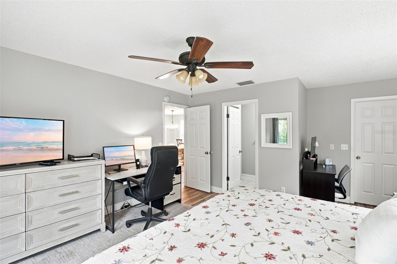 Furnished bedroom with two desk workstations, a floral bedspread, and a ceiling fan.
