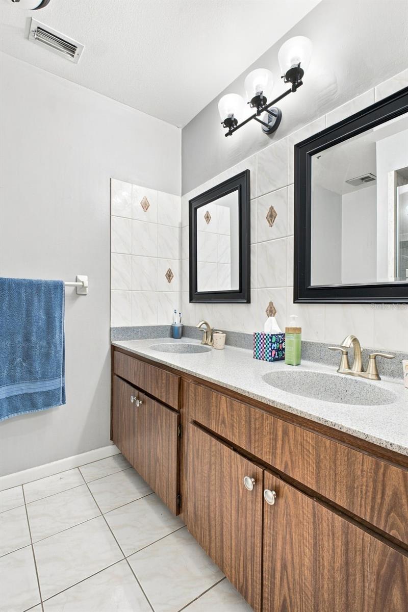 Bathroom with a double-sink vanity, wood-grain cabinets, and two black-framed mirrors.
