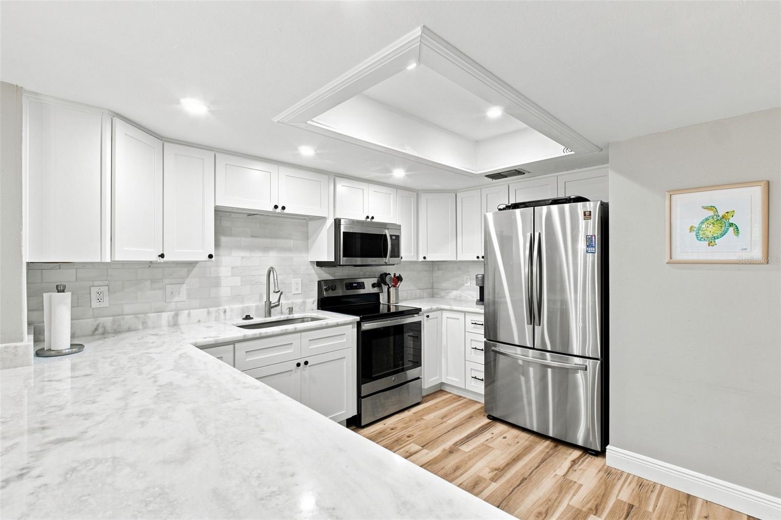Kitchen with white cabinetry, marble-look counters, stainless steel appliances, and light wood floors.