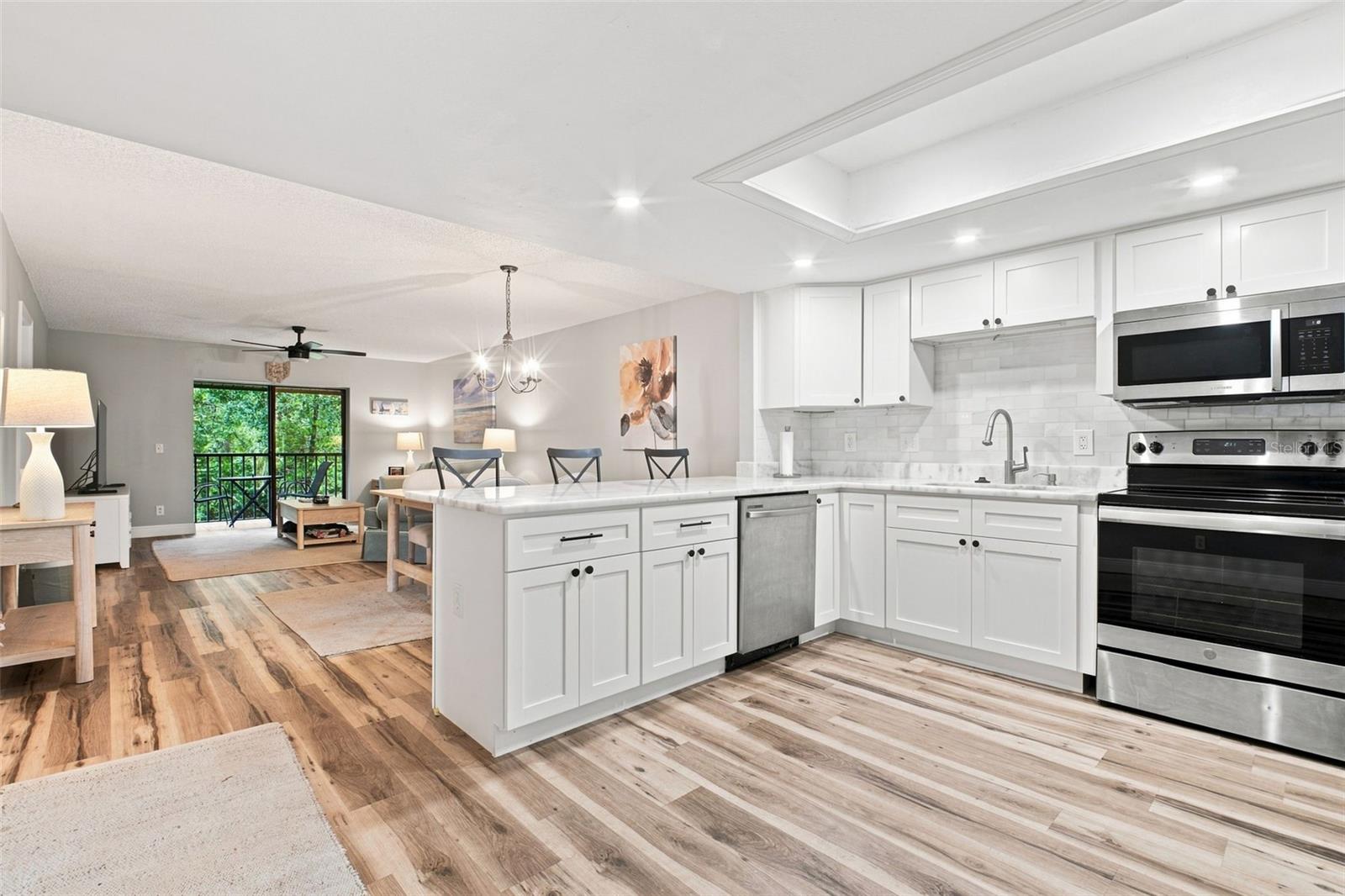 Open kitchen with white cabinetry, a large island, stainless steel appliances, and an adjoining living area.