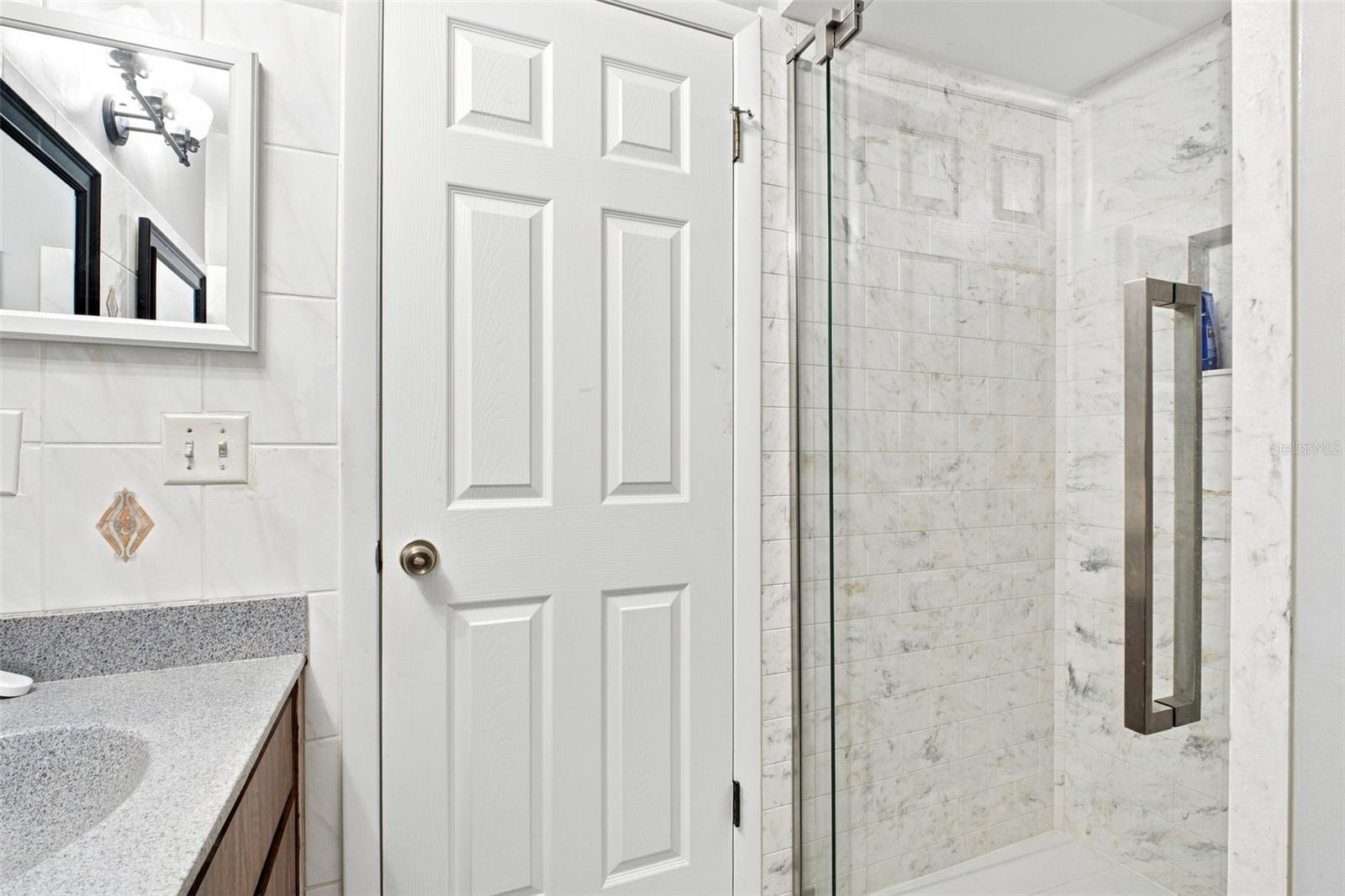 Bathroom with a glass shower enclosure, marble-look tile, and a speckled countertop vanity.