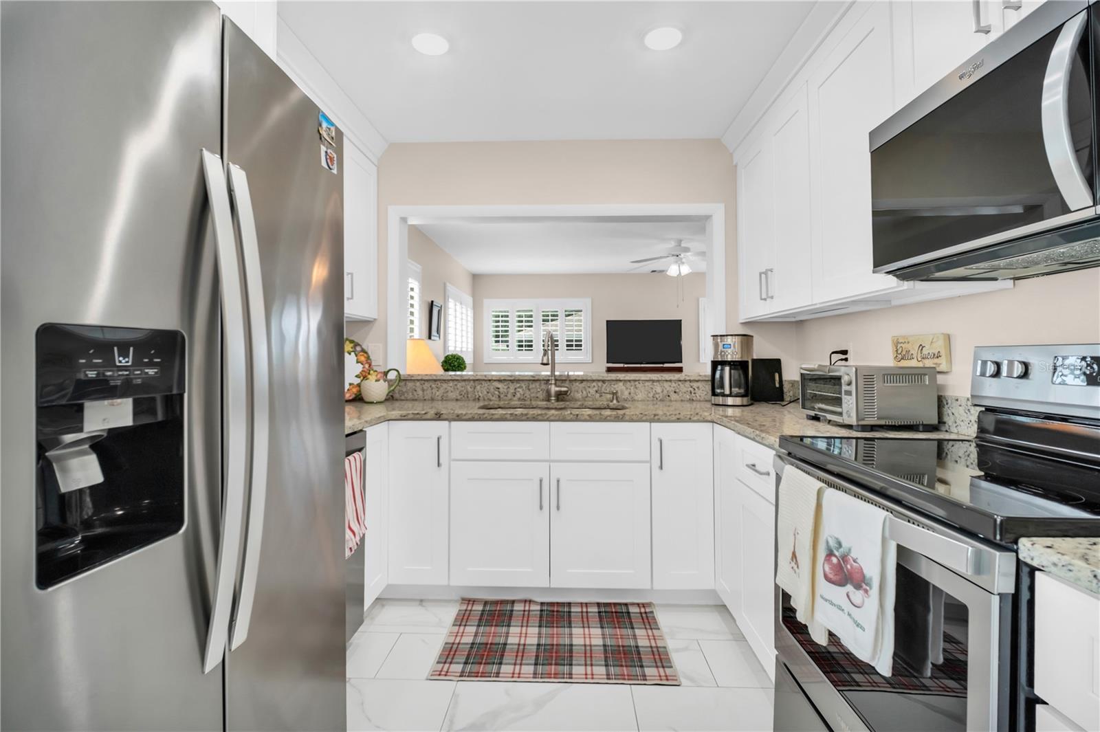 Renovated kitchen with white cabinets, granite counters, stainless steel appliances, and a plaid floor runner.