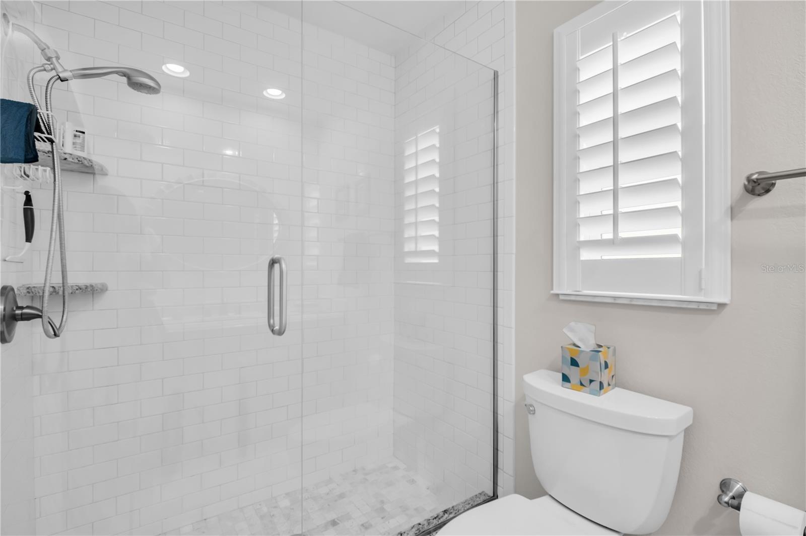 Bathroom with a glass-enclosed subway-tile shower and a shuttered window.
