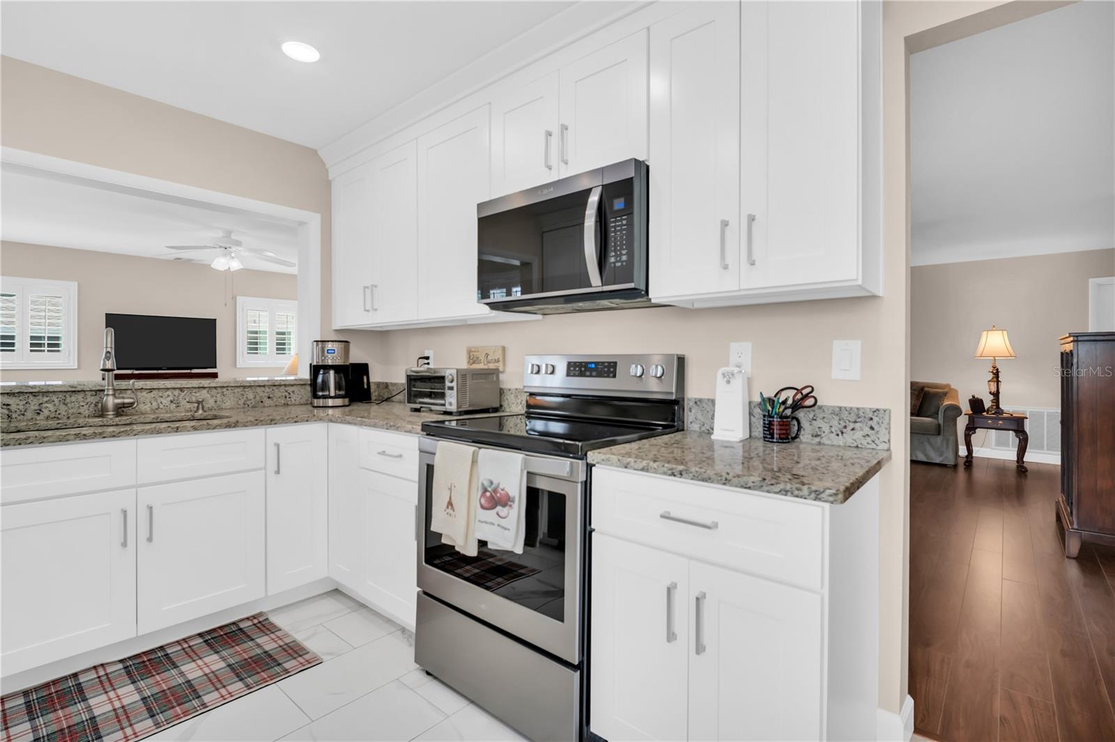 Kitchen with white cabinets, granite counters, and stainless steel appliances opening to a living area.