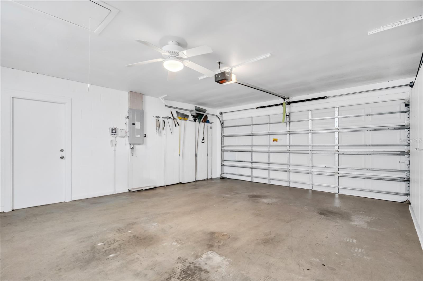 Empty garage with a concrete floor, wall-mounted tools, and a closed white garage door.