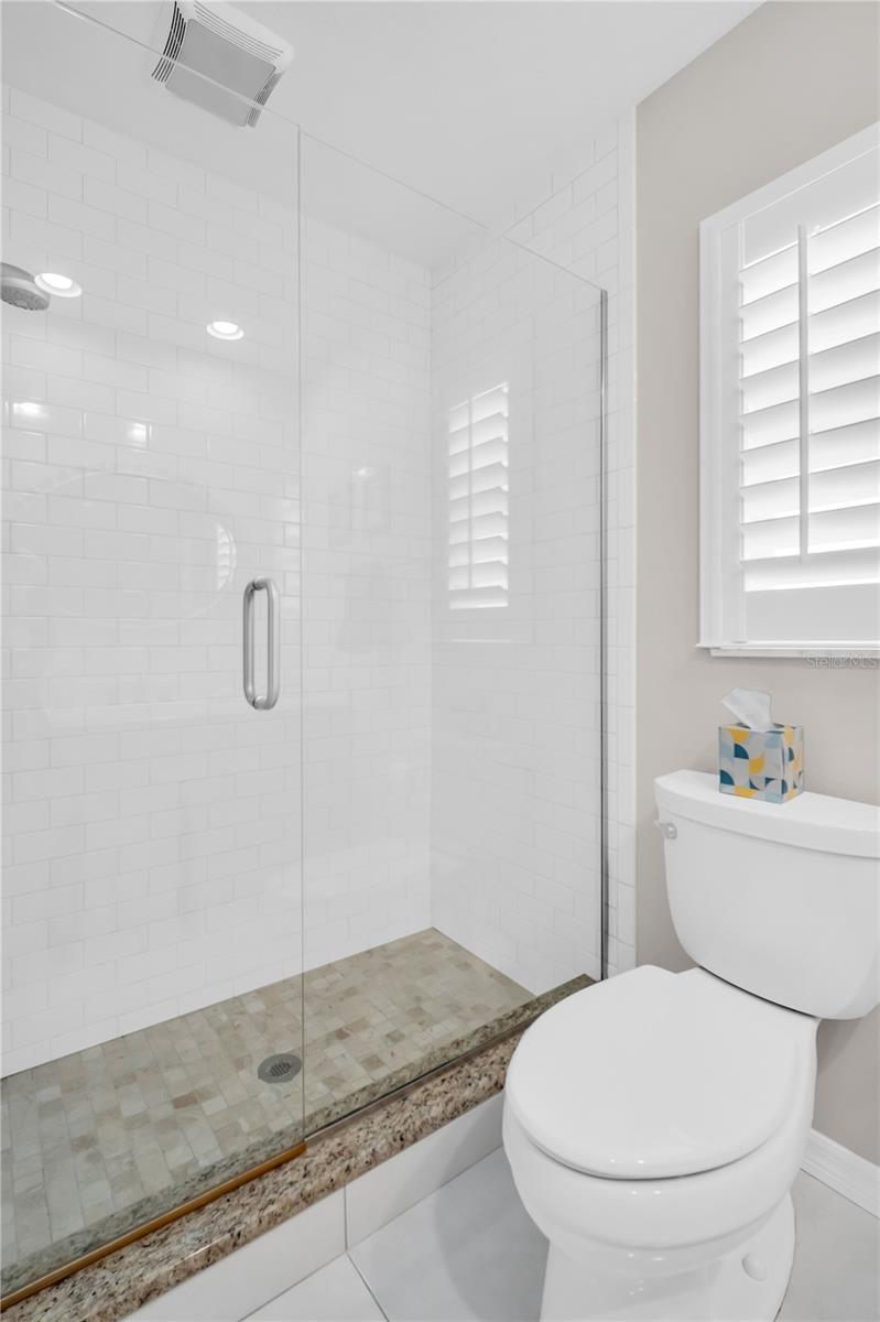 Bathroom with a glass walk-in shower, white subway tile, mosaic floor, and shuttered window.