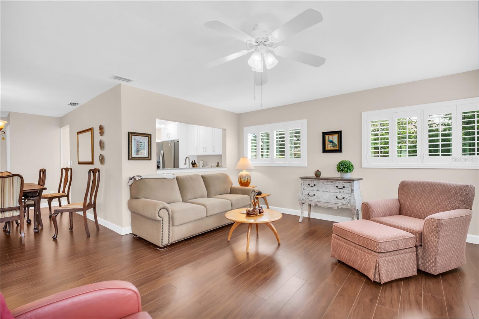 Living room with plantation shutters, wood-look floors, and an opening to the kitchen.
