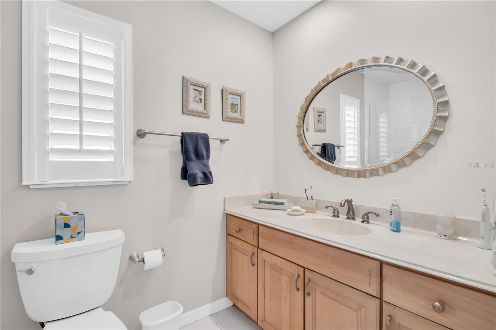 Bathroom with a wood vanity, oval mirror, and shuttered window.