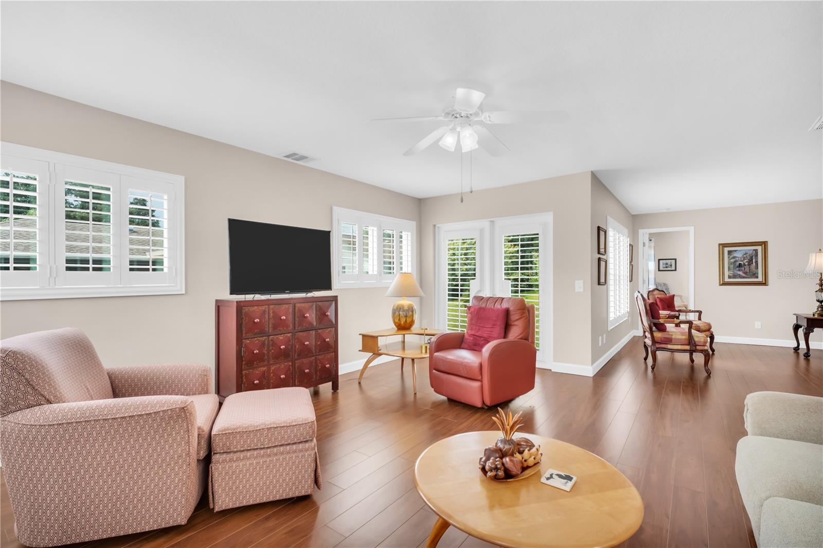 Living room with plantation shutters, wood floors, and red leather seating.