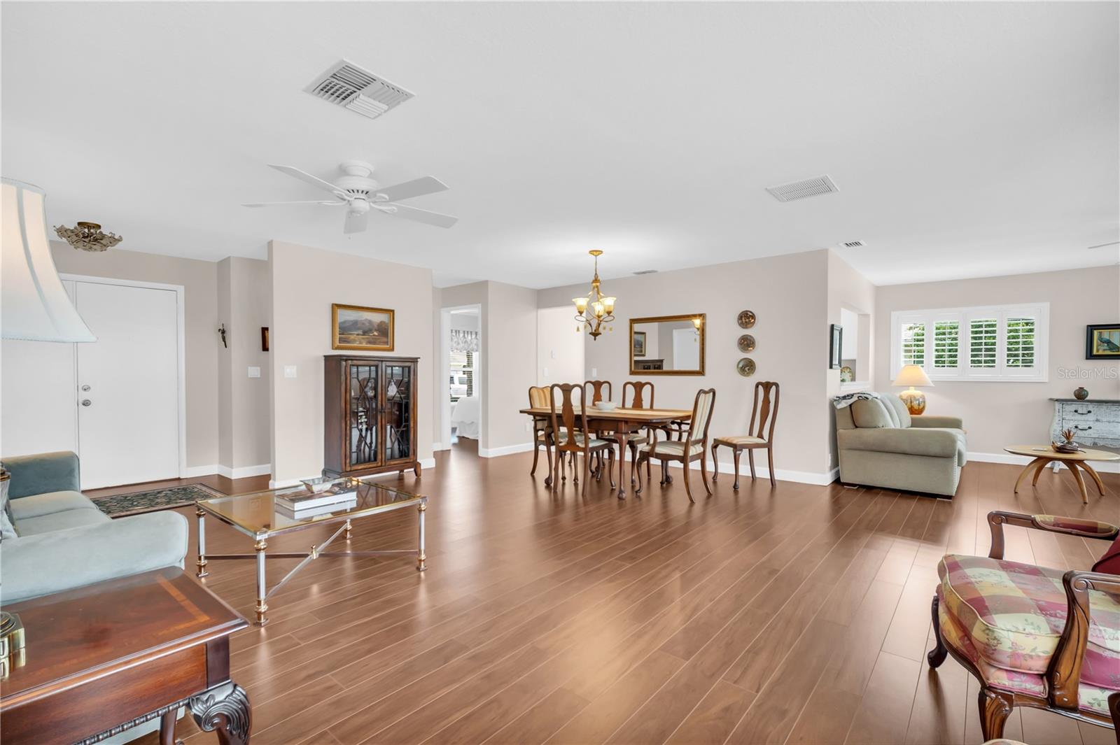 Open living and dining room with wood-look floors, a dining set, and plantation shutters.