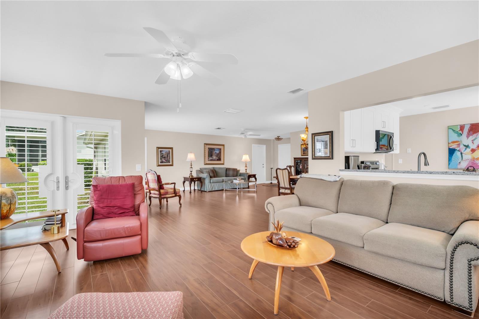 Open-plan living room with a beige sofa, red leather armchair, and shuttered glass doors.