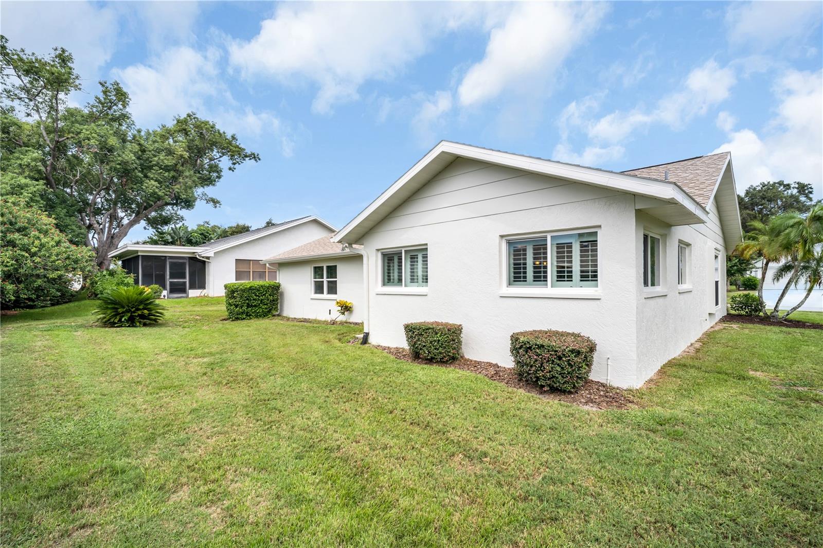 White stucco house with shuttered windows, a gabled roof, and a broad green lawn.