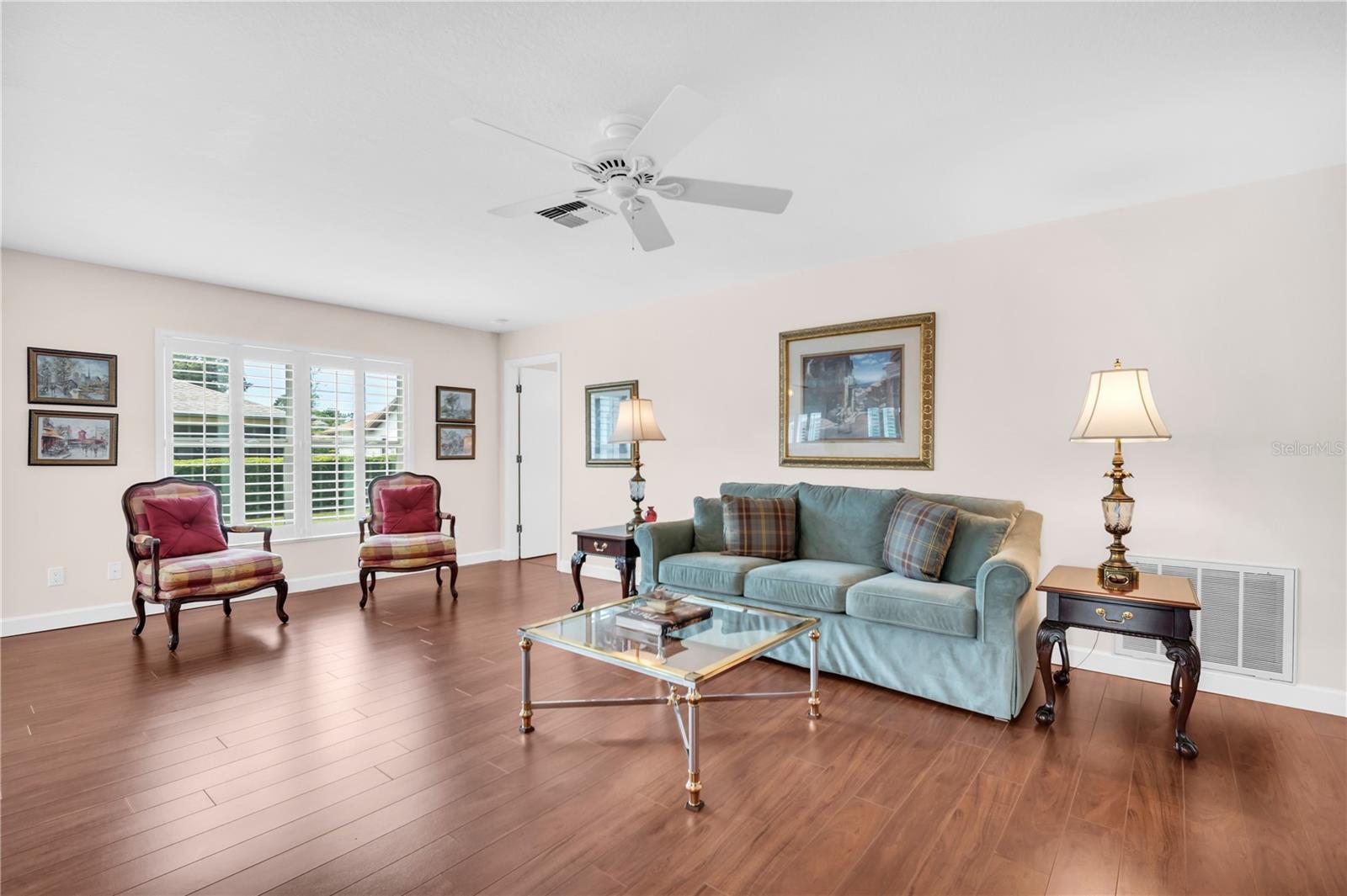 Living room with a blue-green sofa, patterned armchairs, glass coffee table, and hardwood floors.