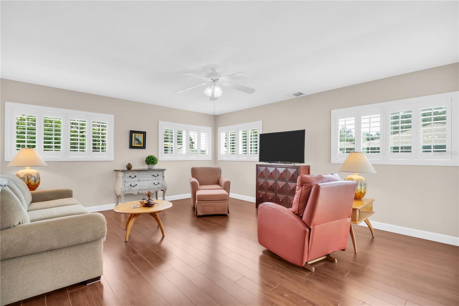 Furnished living room with plantation shutters, wood flooring, and pink leather recliners.