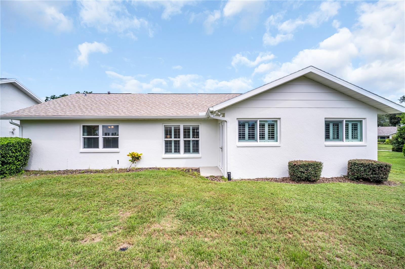 Single-story white stucco home with shuttered windows, trimmed shrubs, and a broad green lawn.