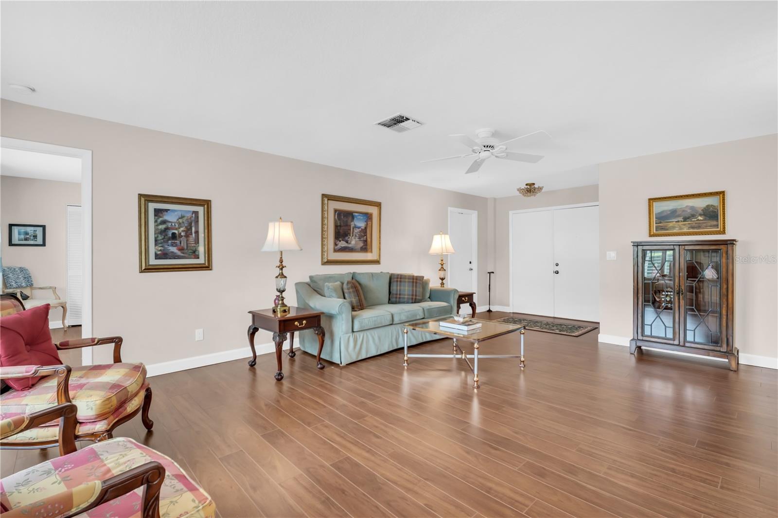 Furnished living room with a pale blue sofa, patterned armchairs, and warm wood-look flooring.