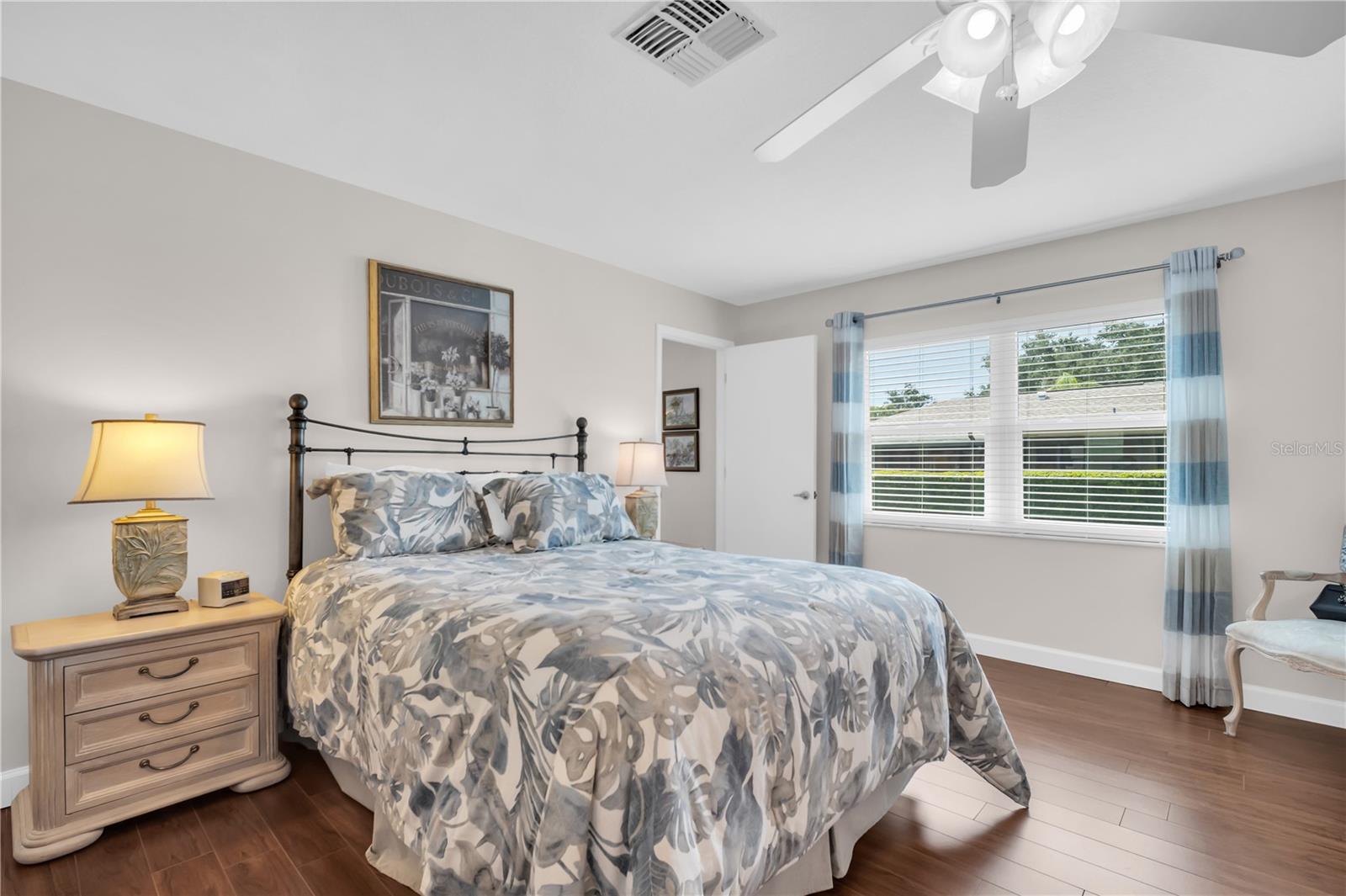 Furnished bedroom with a large floral-bedded bed, blue curtains, and dark wood flooring.