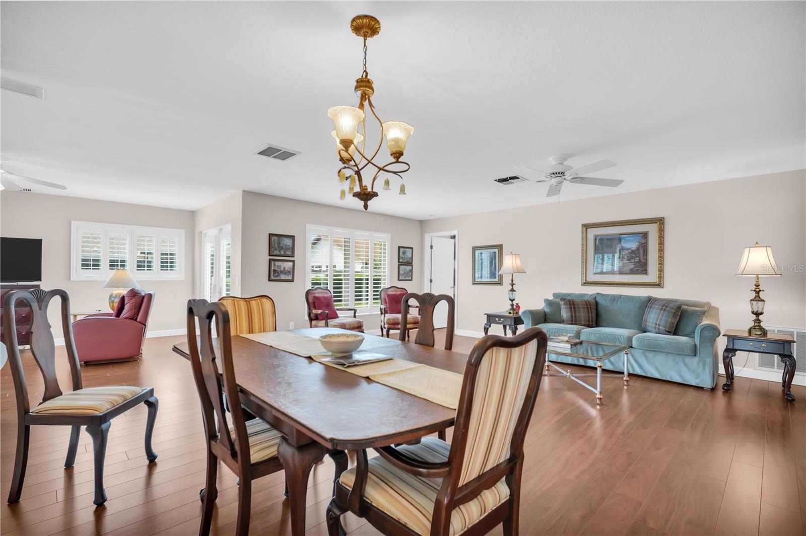 Dining and living room with a wooden table, striped chairs, teal sofa, and brass chandelier.