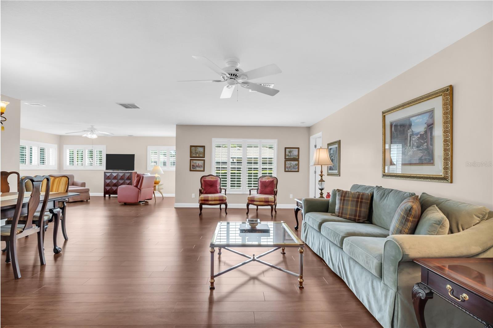 Open living and dining room with plantation shutters, wood-look flooring, and a pale sofa.