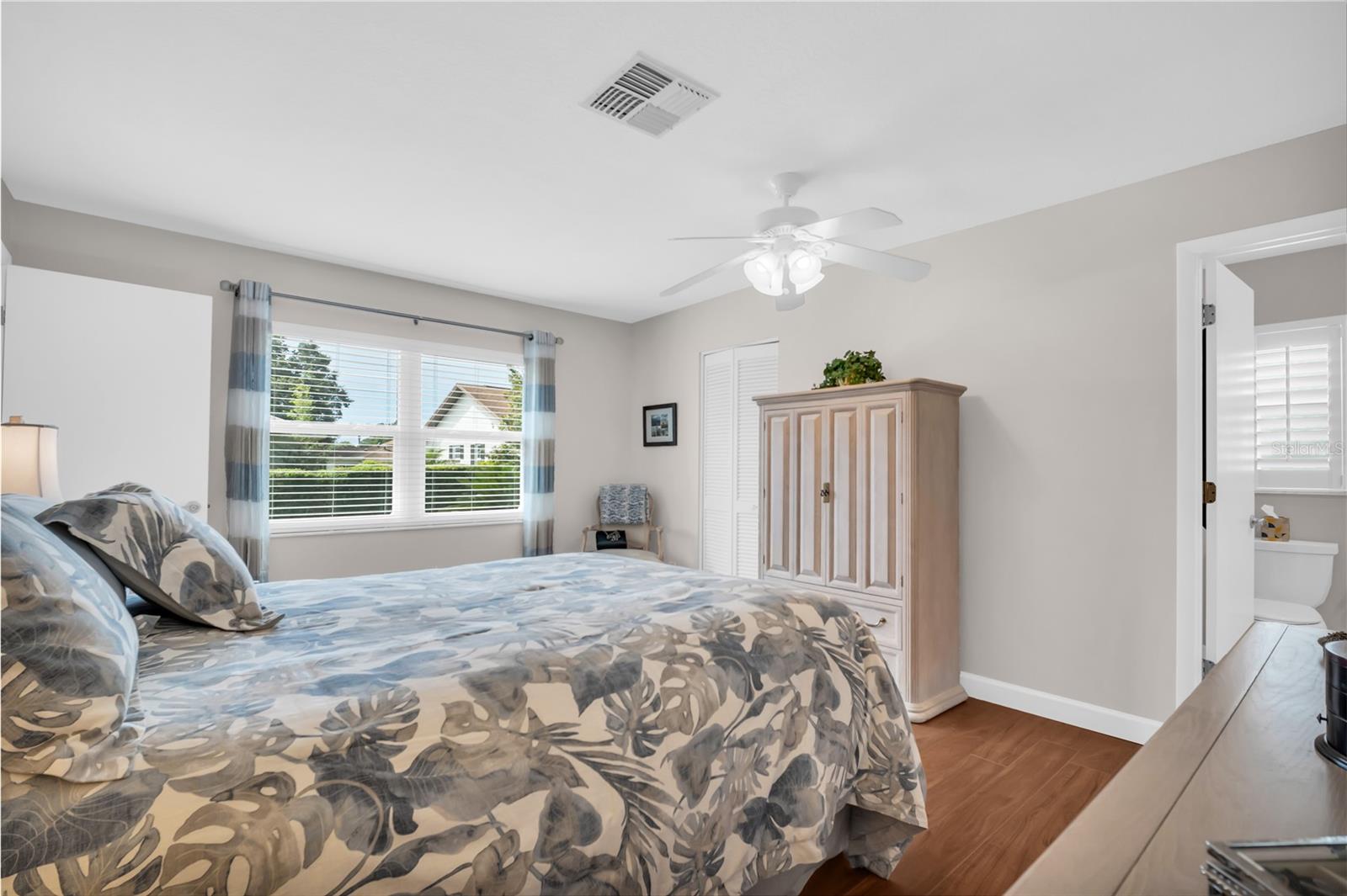 Furnished bedroom with floral bedding, a light wood armoire, and a window with striped curtains.