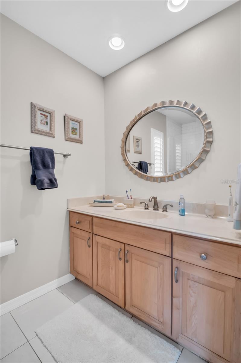 Bathroom vanity with light wood cabinets, an oval mirror, and a navy towel.