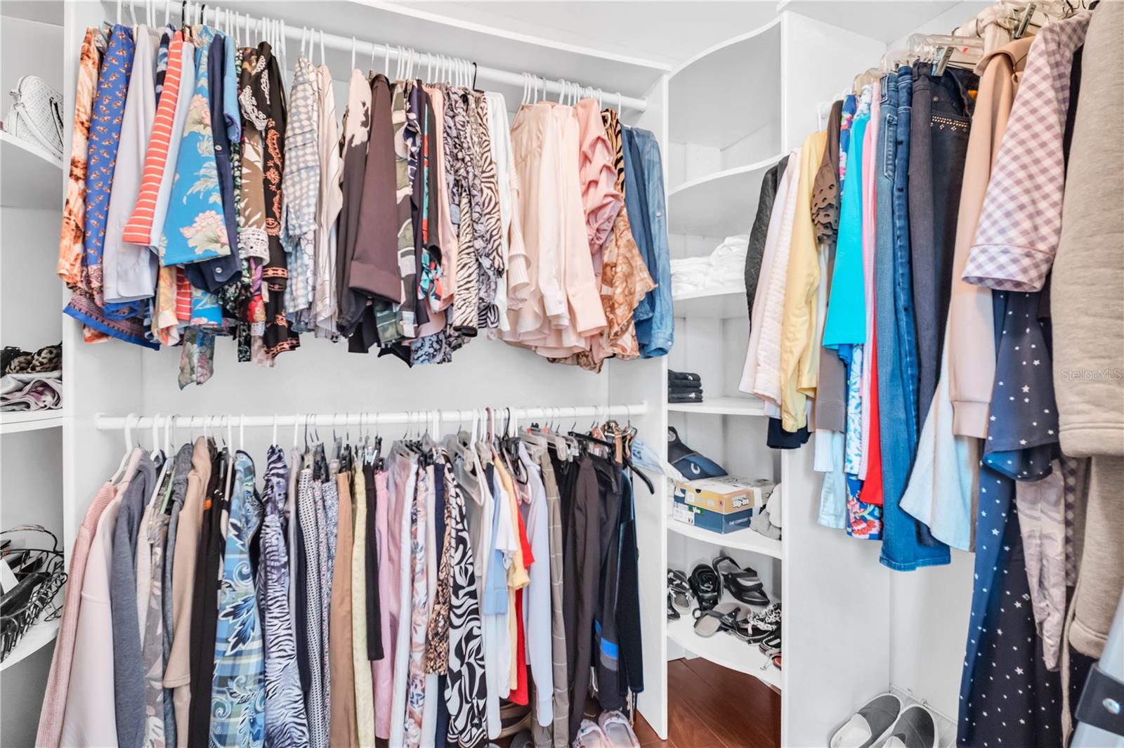 Walk-in closet with built-in shelves, colorful hanging clothes, and shoes.